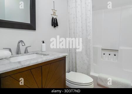 White modern bathroom interior with marble sink, faucet, wood cabinet, and shower with tub Stock Photo
