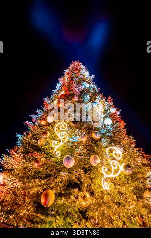 Colorful Christmas tree decorated with ornaments on a dark night sky background, colorful balls, neon lights, laser beams shining in the night sky Stock Photo