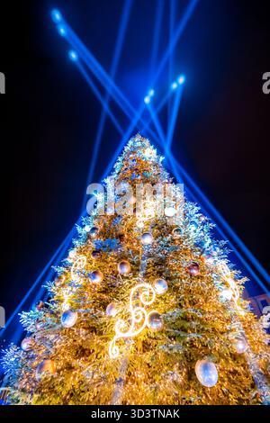 Colorful Christmas tree decorated with ornaments on a dark night sky background, colorful balls, neon lights, laser beams shining in the night sky Stock Photo
