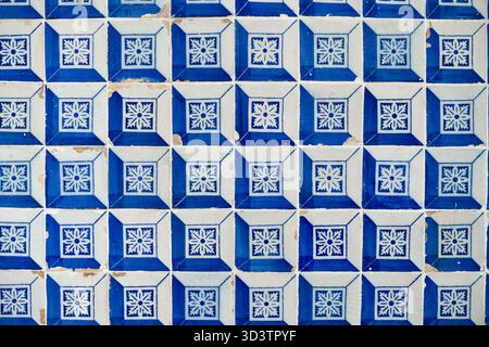 A close-up of a wall covered in traditional Portuguese Azulejo ceramic tiles. The repeating square pattern features blue and white floral-geometric designs, showcasing local art and architecture. Stock Photo
