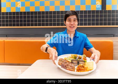 Asian man eat Steak having lunch at a restaurant. Chicken and pork steak with salad cream and Spaghetti, Happy man sitting have dinner enjoying food. Stock Photo