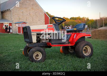 red and white tractor on a farm with a stone barn and pile of hay in the background Stock Photo