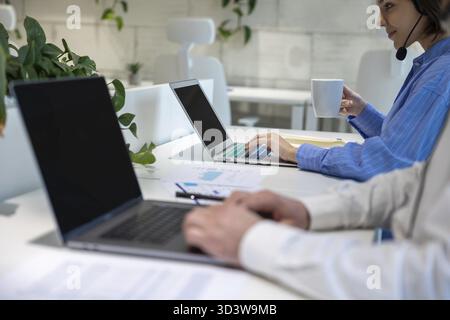 Concentrated female company employee in the headset and her male colleague working on the laptops Stock Photo