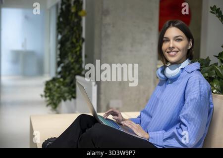 Smiling happy attractive young female remote employee working on the laptop in the business center Stock Photo