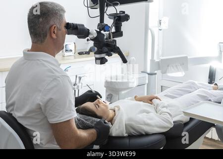 Male dentist using dental microscope treating patient teeth at dental clinic office. Medicine, dentistry and health care concept Stock Photo