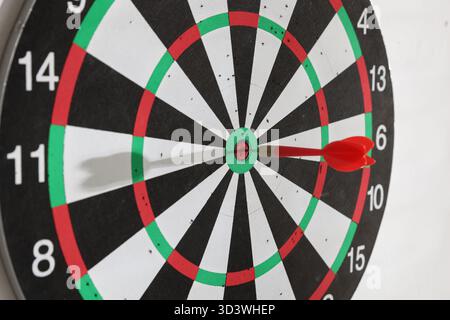 Dartboard with dart on white wall indoors, closeup Stock Photo