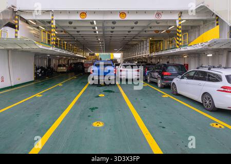 Cars line a ferry deck on a busy vehicle voyage. Green floor, bright yellow markings, and multiple parked cars create a crowded, industrial travel sce Stock Photo