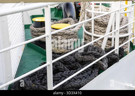 A maritime scene featuring thick rope coils on a green ship deck, white railings, and bright yellow bollards. The arrangement conveys nautical work, s Stock Photo