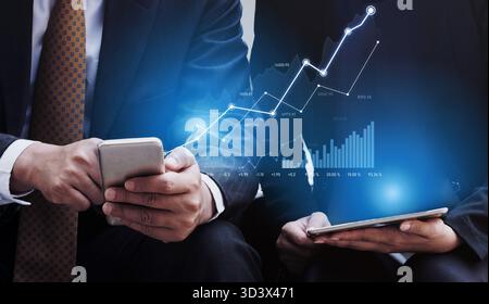 Two business professionals engage with financial data on mobile devices while a growth chart overlays the scene, symbolizing market trends and future Stock Photo