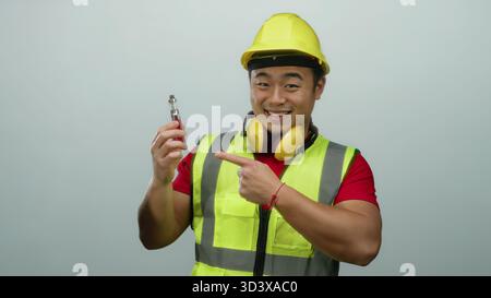 Young man wearing construction gear and a hard hat on white background displays a vape device with a confident smile and thumbs up gesture suggesting Stock Photo