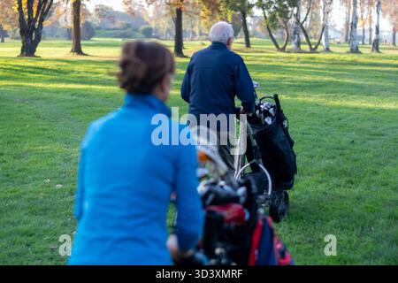 Senior couple walking on a golf course, pushing their golf trolleys and enjoying an active outdoor lifestyle in fall Stock Photo
