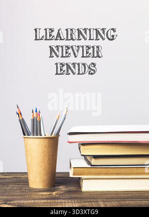 Stack of books and a pencil holder on a table with the words learning never ends written on the wall behind them Stock Photo