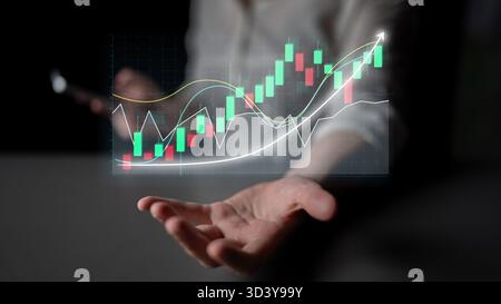 A hand extends towards virtual financial charts displaying market trends, showcasing the intersection of technology and investment in a dynamic Stock Photo