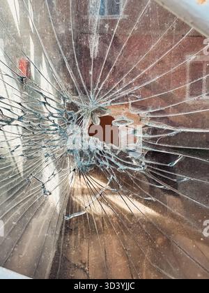 Close-up view of shattered glass displaying intricate cracks and a central hole, highlighting the texture and reflections in a well-lit indoor setting Stock Photo