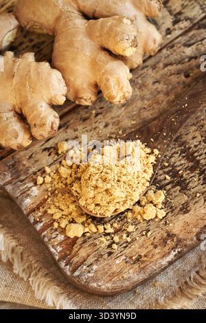 Ground ginger powder on a wooden spoon with fresh ginger root, top view Stock Photo