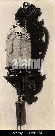 A calendar clock, likely of Dutch origin, from 1636, mounted on a wooden console with intricate woodwork. Photo from 1913. Stock Photo
