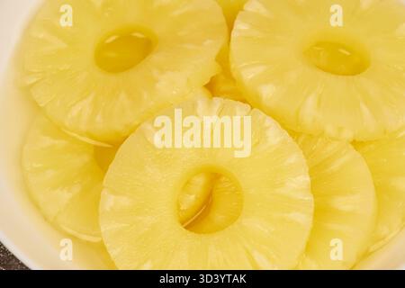 Sliced ​​pineapple, canned preserve. Close-up photograph with copy space on a table against a rustic background. Stock Photo