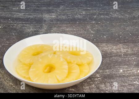 Sliced ​​pineapple, canned preserve. Close-up photograph with copy space on a table against a rustic background. Stock Photo
