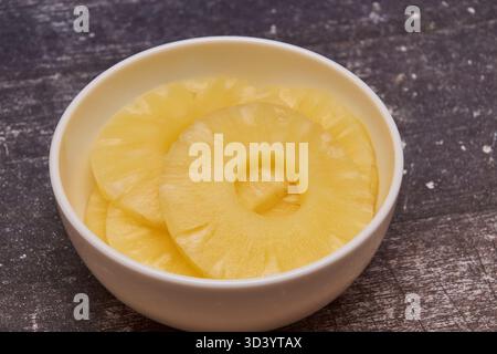 Sliced ​​pineapple, canned preserve. Close-up photograph with copy space on a table against a rustic background. Stock Photo