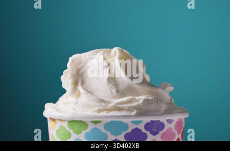 white soft vanilla ice cream in paper cup, food closeup on blue background Stock Photo