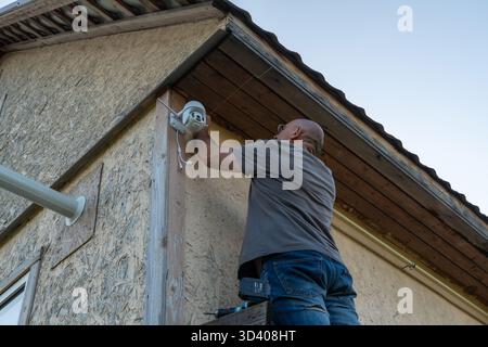 Adult male installing security camera on house exterior for home safety Stock Photo