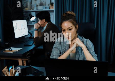 Serious face of thinking businesswoman focusing computer to report data analysis social media online project job with coworker working at back side at Stock Photo