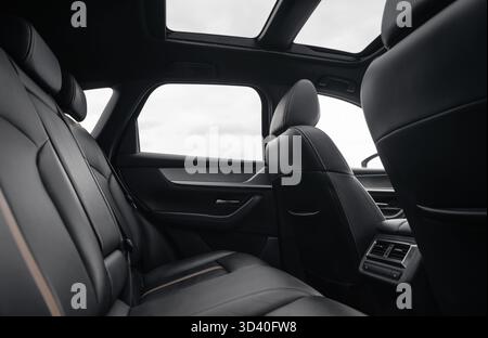 Rear row of seats in a car. SUV or wagon interior with black leather seats and panoramic glass roof, cloudy autumn sky in the background. Stock Photo