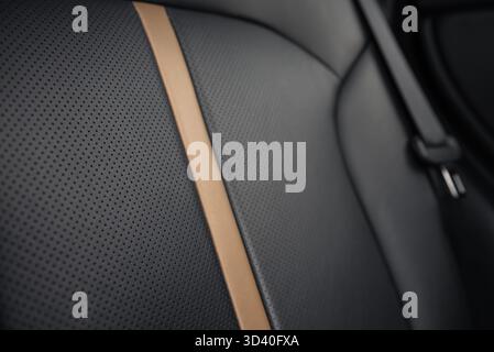 Car leather seat - close-up view. Modern car's black rear leather seat with perforated leather and vertical beige stripe - selective focus. Stock Photo