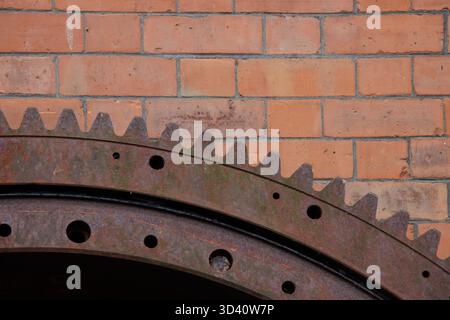 Large rusty industrial metal cog wheel and red brick wall Stock Photo