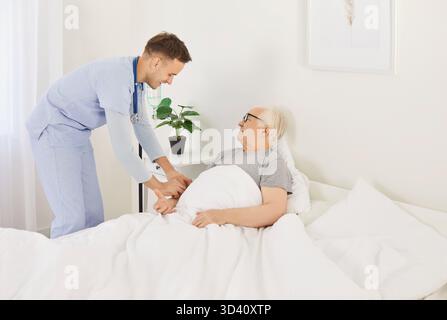 Nursing support sick senior man with intravenous drip lying on medical couch at home, clinic  Stock Photo