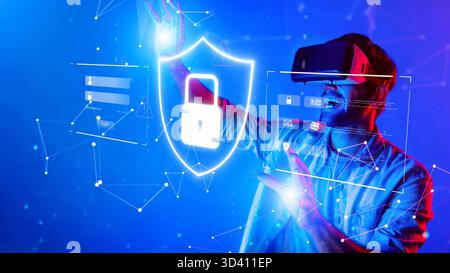 A man wearing a virtual reality headset interacts with digital elements representing data protection and security in a dynamic blue environment Stock Photo