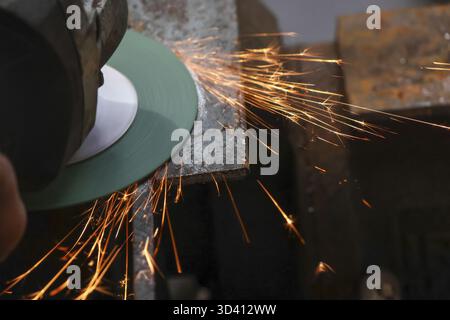 Close up of worker using an angle grinder to cut metal, creating bright sparks. industrial process shows focused and intense scene in workshop Stock Photo