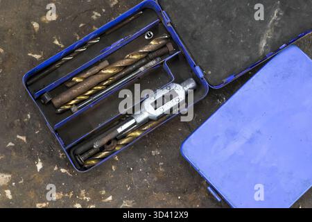 Professional tap and die set with metal drill bits and wrench, neatly organized inside blue tool kit, ready for precision work on workshop floor Stock Photo