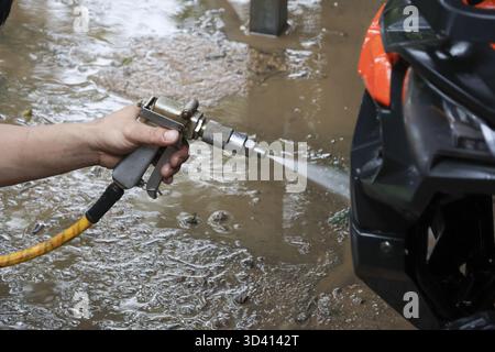 Worker hand cleaning black car with high pressure water gun spray. Focused manual labor at car wash service, detailing dirty automobile for maintenanc Stock Photo