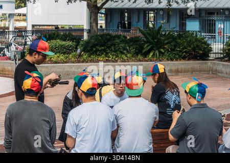 Group of friends enjoying a sunny day at the park while wearing colorful hats and sharing laughter together at Disney Springs, Florida Stock Photo