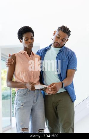 Reading Diverse couple standing together in bright modern home interior, holding letter envelope Stock Photo