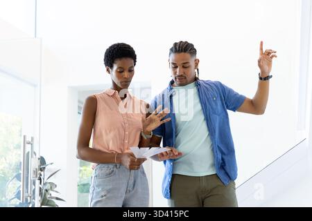 Diverse couple examining printed papers in bright modern entryway, with documents in hand Stock Photo