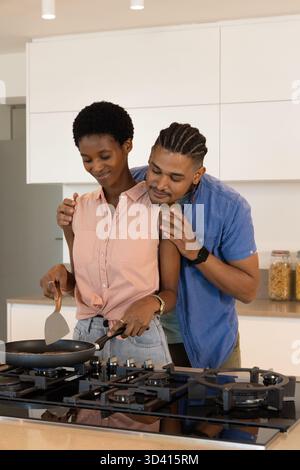 Cooking Diverse couple hugging at gas stove in modern kitchen, with nonstick pan and clear jars Stock Photo