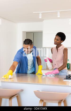 Diverse couple cleaning island countertop in modern kitchen, with cloths and spray bottle Stock Photo