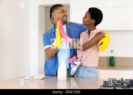 Wearing gloves, diverse couple cleaning countertop in home kitchen, with spray bottle and cloths Stock Photo
