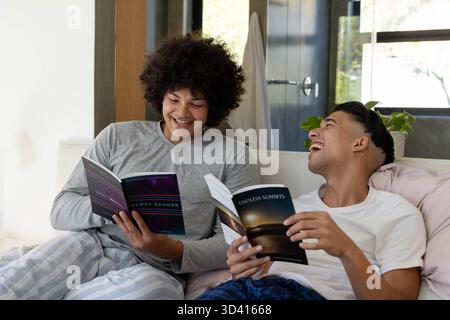 Diverse male friends laughing and reading glossy magazines on sofa at home, with potted plant Stock Photo