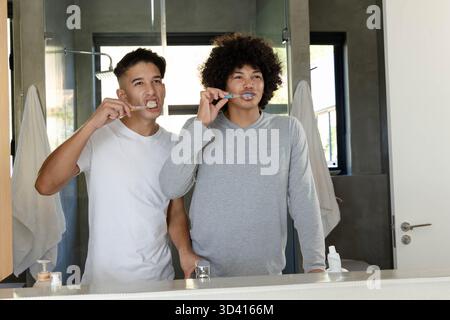 Brushing teeth Diverse male friends standing at modern bathroom sink, with toothbrushes and towels Stock Photo