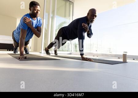 Doing one-arm push-ups, African American men exercising on mats in home gym with water bottle Stock Photo
