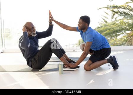 Exercising African American men performing sit-ups on exercise mat in home gym, with water bottle Stock Photo