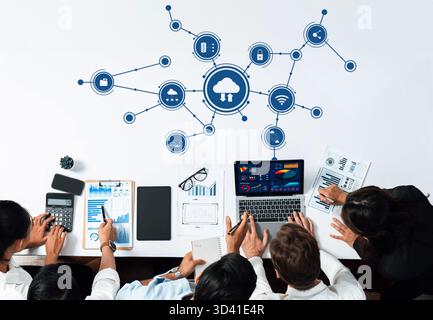 A diverse team collaborates in a modern workspace, surrounded by technology symbols. They analyze data on laptops while leveraging cloud connectivity Stock Photo