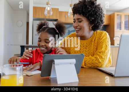 Helping Diverse family doing homework at kitchen table, with tablet on stand and pencil Stock Photo