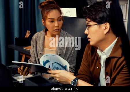 Serious face of working sales manager discussing on report data analysis paperwork with coworker at over late night at modern office, focusing on Stock Photo