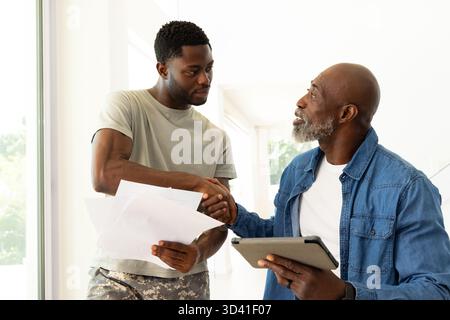 Shaking hands African American colleagues near window in modern hallway, with tablet and papers Stock Photo