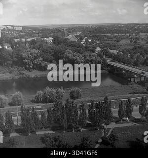 An archival high-angle view from July 1997, showing the Torets River and its embankment in Sloviansk, Ukraine. The wide river flows through the city. On the right, a road bridge crosses the water, connecting different parts of the city. In the foreground, a road is lined with tall poplar trees. This panoramic view captures the urban and natural landscape of the post-Soviet city. This is a moment of everyday life in the peaceful Donbas before the war. Stock Photo