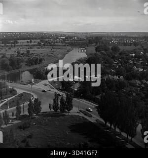 An archival high-angle panorama from July 1997, showing the embankment area of the Torets River in Sloviansk, Ukraine. The view captures a busy road bridge with car traffic crossing the river on the left, and a road intersection below. The winding river flows through a landscape of dense green trees. In the distance, a second, arched bridge is visible. This photo shows the city landscape in the post-Soviet 1990s. This is a moment of everyday life in the peaceful Donbas before the war. Stock Photo